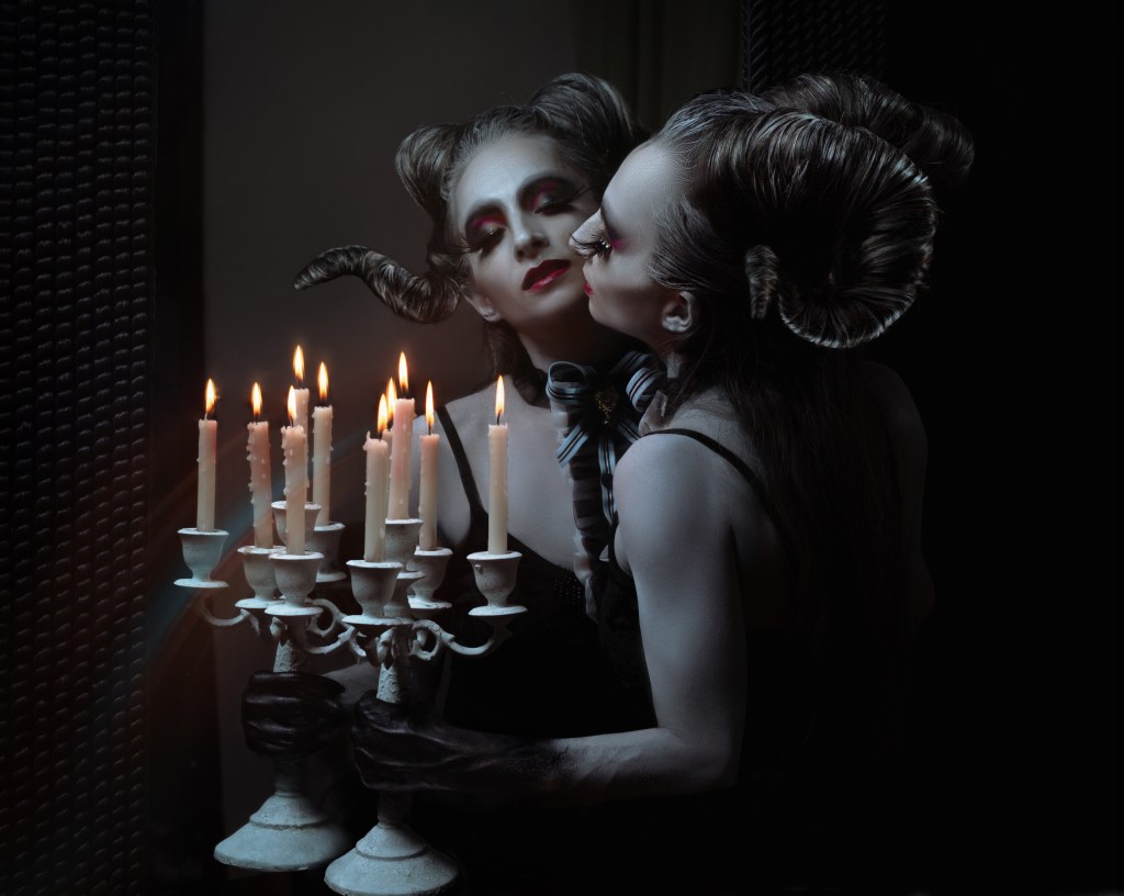 Joanne Froggatt dressed as a beautiful horned Halloween monster looking into a mirror and holding a candle in the dark